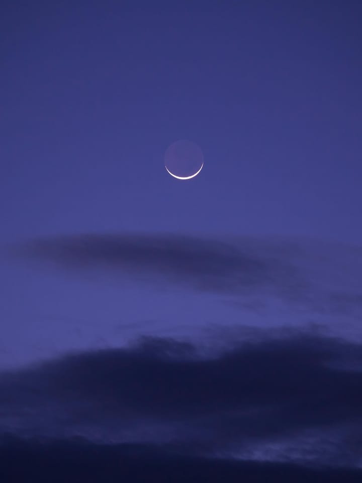 waxing crescent moon tipped up like horns, bright in a cloudy purple sky