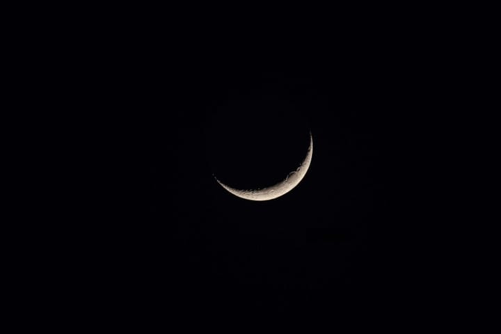 grey crescent moon with visible craters against a solid black sky