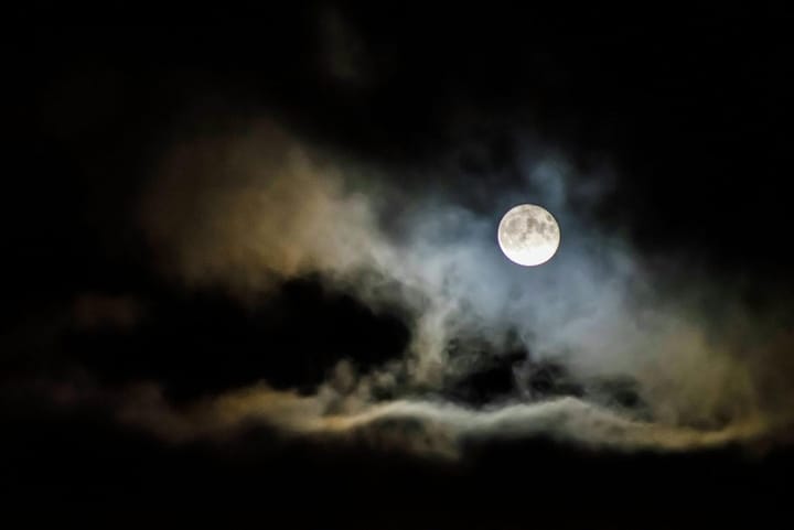 a full moon with a thin cloud cover, white with a little pale sunset peach on one side, in a black sky