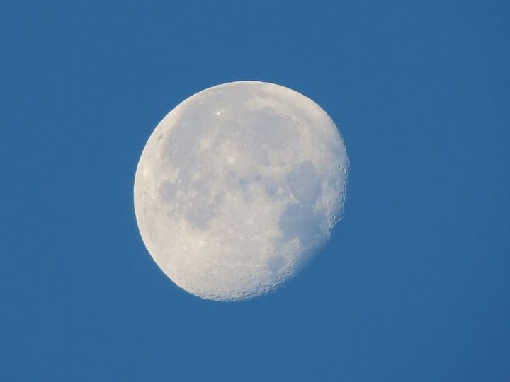bone-white, pockmarked waning gibbous moon in a clear, slat-blue sky