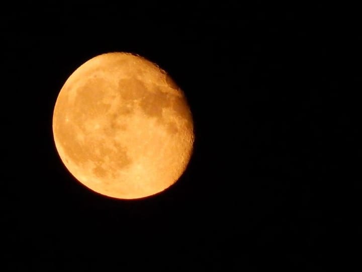 waning gibbous moon, recently full, glows orange in a pitch-black sky